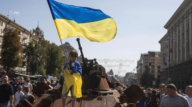 a boy waves a national flag atop of armoured personal carrier