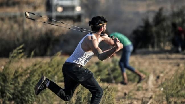 a palestinian protester uses a slingshot throw a stone in gaza