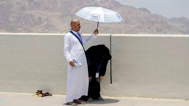 a pilgrim holds an umbrella as his wife prays