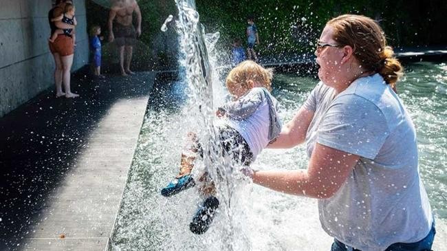 a woman holds a young child under a waterfall