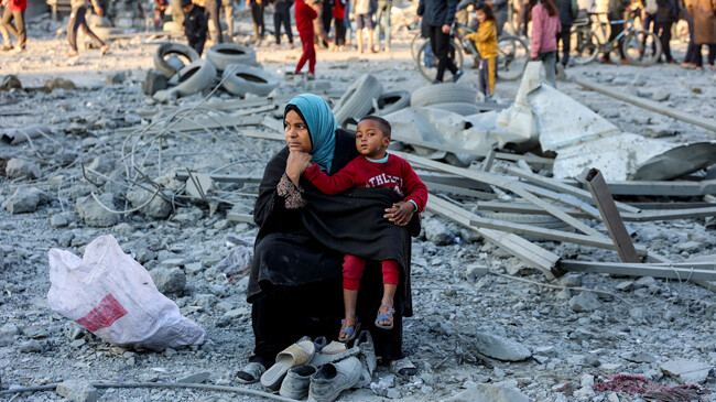 a woman sits with a child amid debris and rubble in gaza city