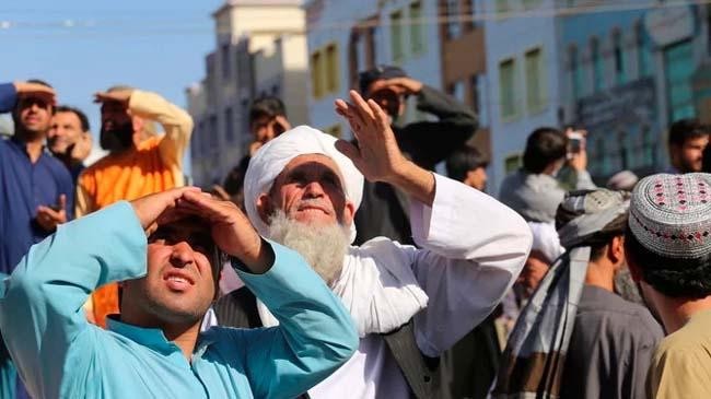 people look up at a dead body hanged by the taliban